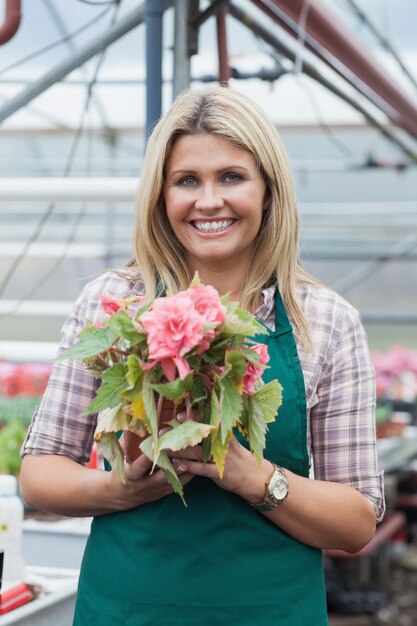 Blondevrouw die een bloem houden die in tuincentrum werken