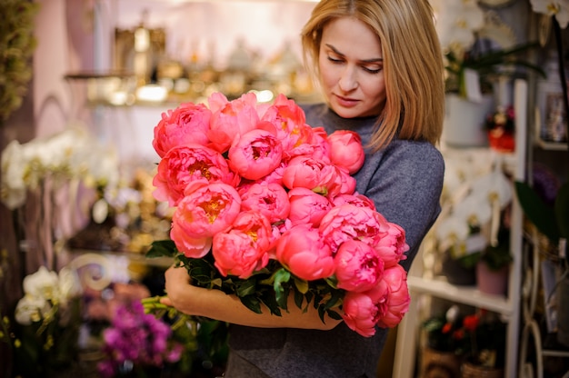 Blondevrouw die een groot boeket van roze pioenen houden