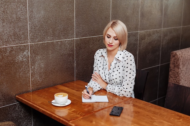 Blondevrouw die in koffie in notitieboekje schrijven