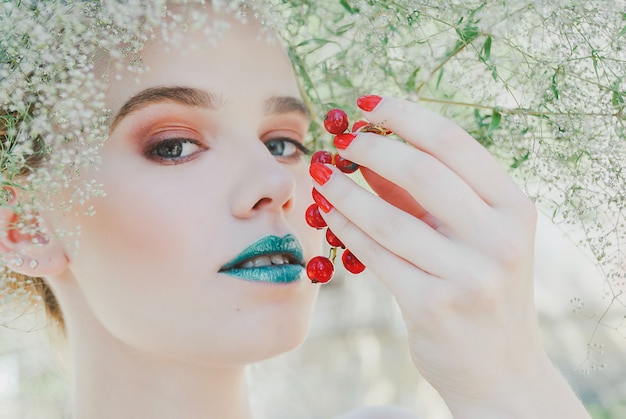 Blondevrouw die met groene lippen rode aalbibos houden. concept van moeder natuur