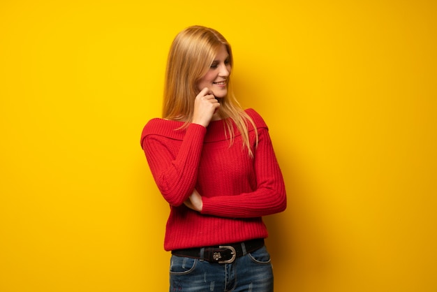 Blondevrouw die over gele muur aan de kant met de hand op de kin kijken