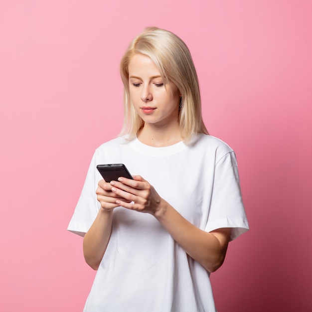 Blondevrouw in witte t-shirt met mobiele telefoon op roze
