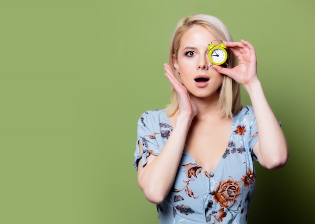 Blondevrouw met wekker op groene muur