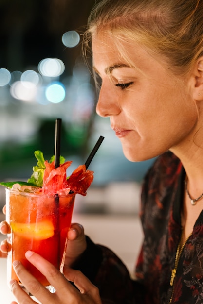 Foto blondevrouw ongeveer om een rode cocktail met een stro bij nacht te drinken