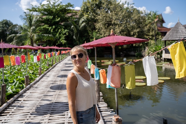 Blondevrouw op een houten brug die een vijver met gekleurde paraplu's onder ogen zien