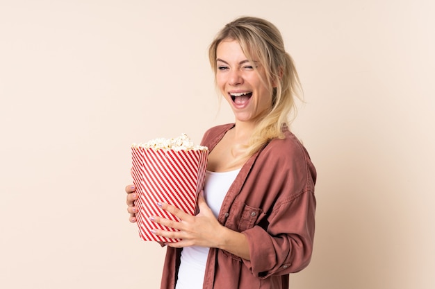 Blondevrouw over geïsoleerde muur die een grote emmer popcorns houdt