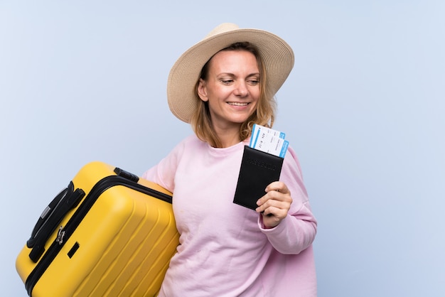 Blondevrouw over geïsoleerde muur in vakantie met koffer en paspoort