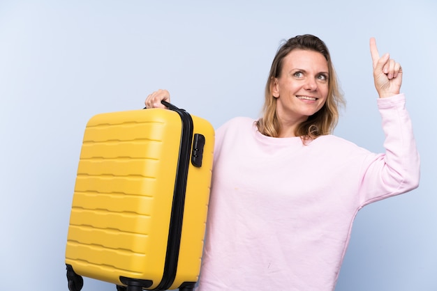 Blondevrouw over geïsoleerde muur in vakantie met reiskoffer en het benadrukken