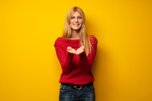 Foto blondevrouw over gele muurholding copyspace denkbeeldig op de palm om een advertentie op te nemen