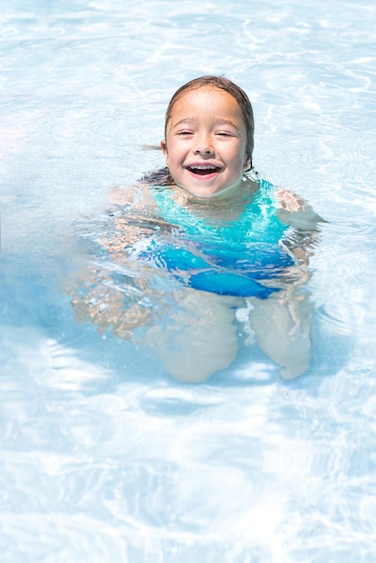 Blondharig meisje in een zwembad glimlachend genietend van zichzelf in het water Zwembad zwempak kinderen zomer ontspannen vakantieoord en reisconcept