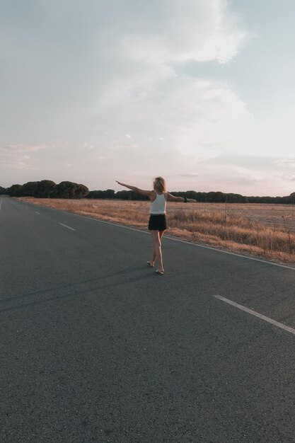 Blondharige vrouw loopt op de weg bij zonsondergang in korte broek