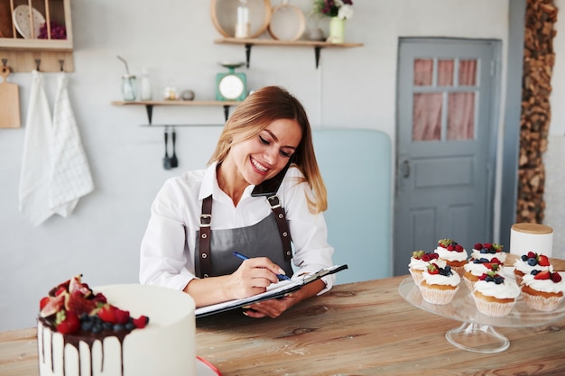 Blondje neemt telefonisch een bestelling op. zelfgemaakte koekjes en taart op tafel.