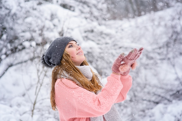 ブロンディの女の子は冬の森で雪をキャッチします。