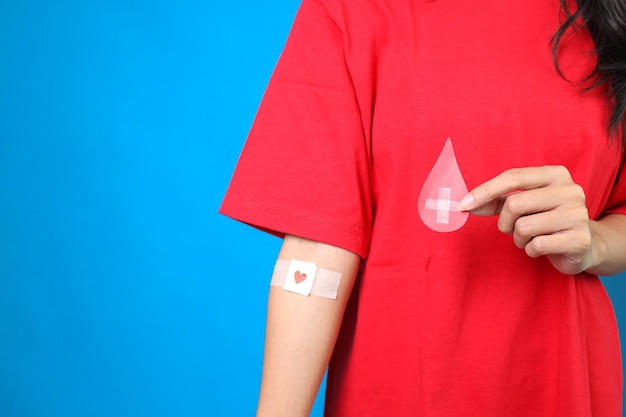 blood donor with bandage after giving blood holding blood drop paper cute on blue background
