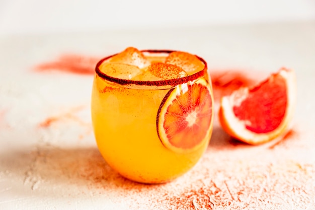 昔ながらのグラスにブラッドオレンジのマルガリータカクテル、縁にスモークパプリカ、ピンクグレープフルーツ。