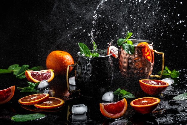 Blood orange Moscow mule alcohol cocktails with fresh mint leaves and ice in copper mugs splashes and ice frozen motion