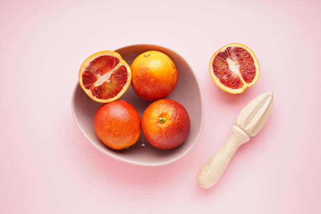 Blood oranges and a wooden juicer on a pink background top view