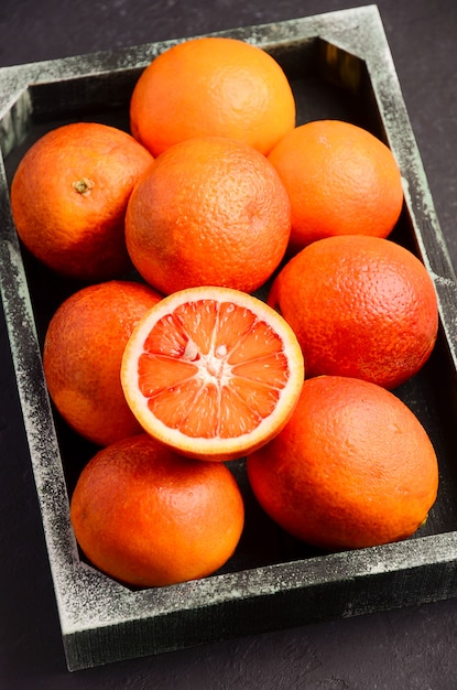 Blood oranges in wooden tray on dark  .