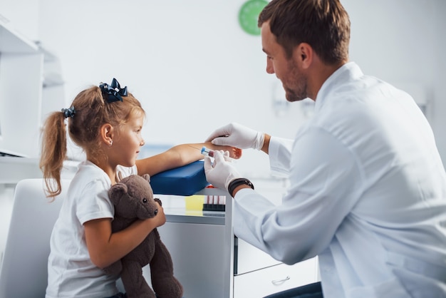 Blood sampling. Little girl with her teddy bear is in the clinic with doctor.