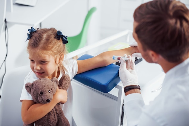 Blood sampling. Little girl with her teddy bear is in the clinic with doctor.