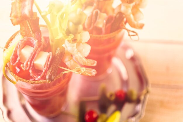 Bloody mary cocktail garnished with celery sticks, olives, and bacon strips.