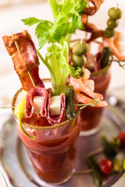 Bloody mary cocktail garnished with celery sticks, olives, and bacon strips.