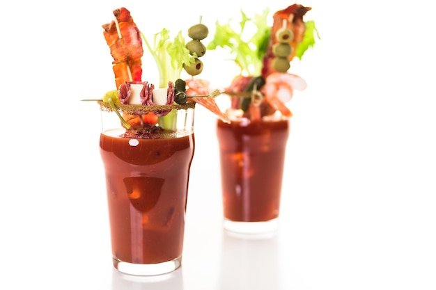 Bloody mary cocktail garnished with celery sticks, olives, and bacon strips.