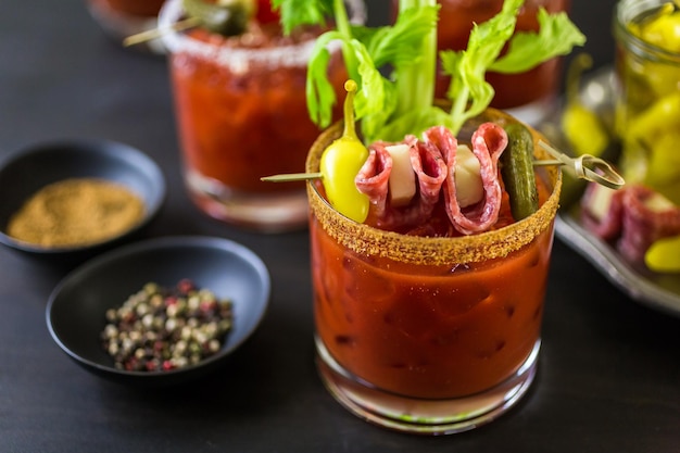 Cocktail di bloody mary guarnito con bastoncini di sedano, olive e striscioline di pancetta.