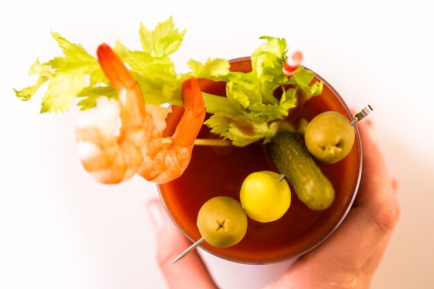 Bloody mary cocktail garnished with olives, pickles, and cocktail shrimp on a white background.