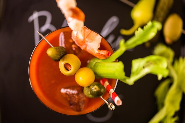 Photo bloody mary cocktail garnished with olives, pickles, and cocktail shrimp.