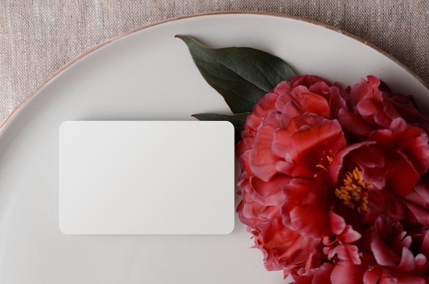 Blooming branches with peony flowers and buds Blank business card mockup on ceramic plate