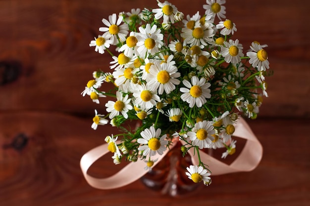 Blooming fresh camomiles bouquet with ribbon bow on wooden background Beautiful chamomile flowers with green leaves