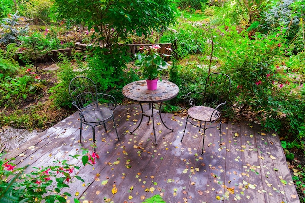 Цветущий сад во дворе загородного дома с двумя стульями и столом
