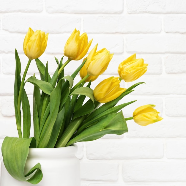 Fioritura di fiori gialli in vaso bianco su sfondo decorativo muro di mattoni con copia. fiori primaverili per la festa della donna o della mamma.