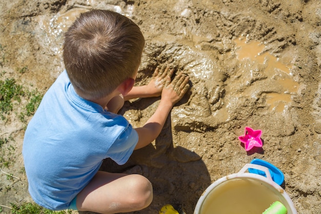 Blootvoets kind spelen met nat zand. Kleine jongen kneedt en modelleert modder op zonnige zomerdag.