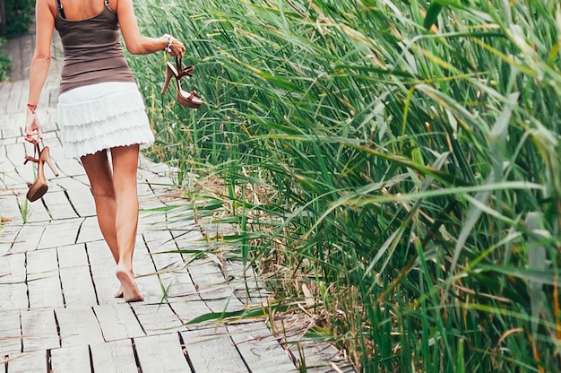 Blote voeten mooie vrouwelijke fit benen met schoenen met hoge hakken in handen weglopen groen gras rond