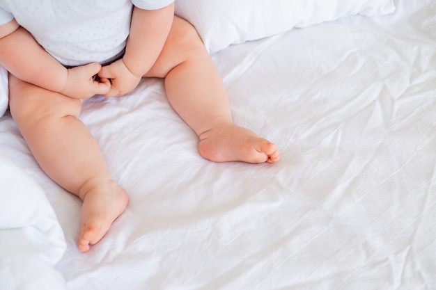 blote voeten van een baby zittend op een wit laken op het bed close-up bovenaanzicht