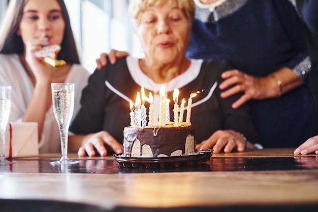 ろうそくを吹く。屋内で誕生日を祝う家族や友人と年配の女性。