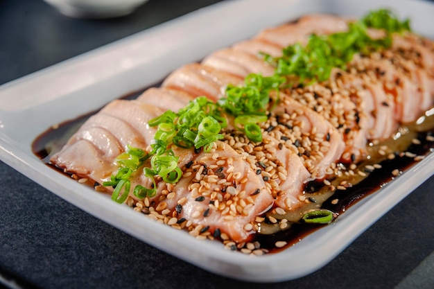 Blowtorcherd salmon sashimi with sesame, shoyu and passion fruit sauce on a black table. Closeup.