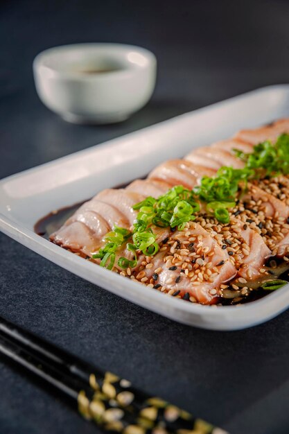 Blowtorcherd zalmsashimi met sesam, shoyu en passievruchtsaus op een zwarte tafel. Detailopname.