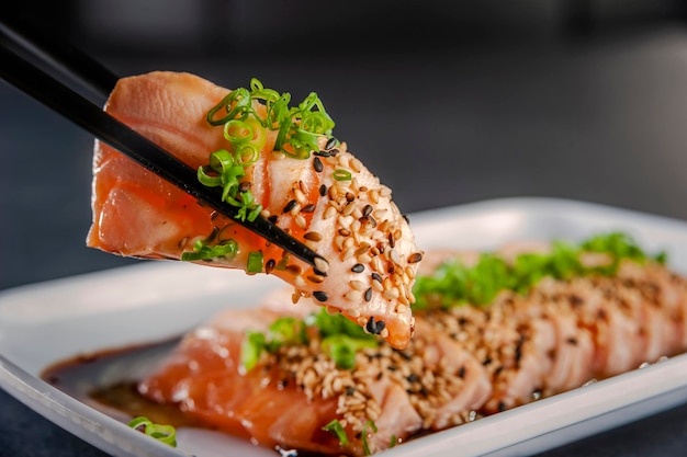 Blowtorcherd zalmsashimi op stokjes met sesam, shoyu en passievruchtensaus op een zwarte tafel.