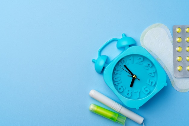 Blue alarm clock, female hygienic pad and tampon, top view