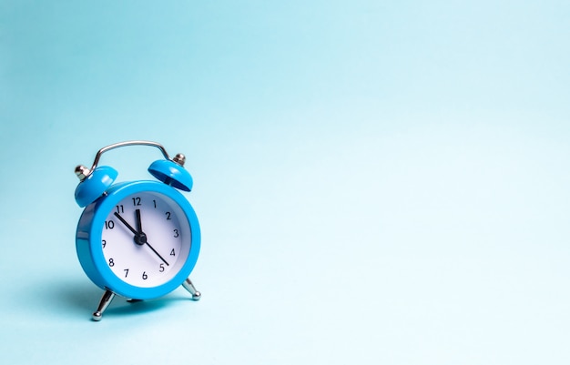 A blue alarm clock on a light blue background. The concept of waiting for a meeting, a date.