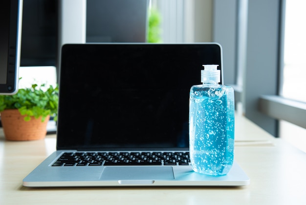 ノートパソコンに置いた手洗い用の青いアルコールジェルボトル