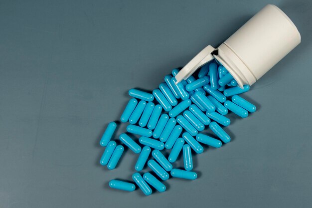 Фото Текстура синих капсул с антибиотиками и белой бутылкой фармацевтическое производство глобальное здравоохранение устойчивость к антибиотикам таблетки в желатиновых капсулах