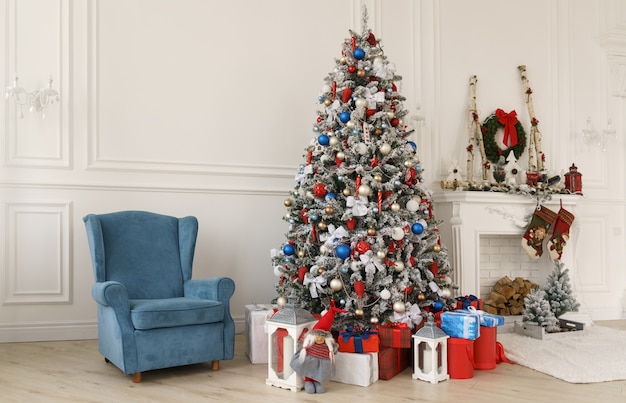 Blue armchair and gift boxes under decorated Christmas tree beside decorated fireplace