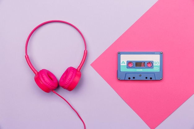 Синяя аудиокассета на розовых и розовых наушниках на сиреневом фоне