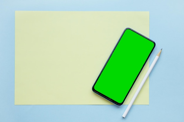 On a blue background a blank sheet of paper a phone with a green screen and a pencil