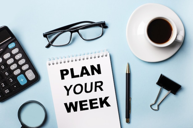 On a blue background, glasses, calculator, coffee, magnifier, pen and notebook with the text PLAN YOUR WEEK