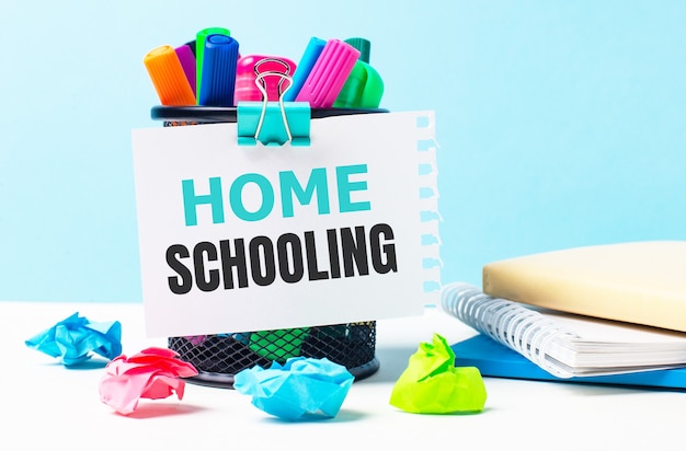 On a blue background - a stand with bright markers, notepads and multi-colored crumpled pieces of paper. A sheet of paper with the text HOME SCHOOLING.